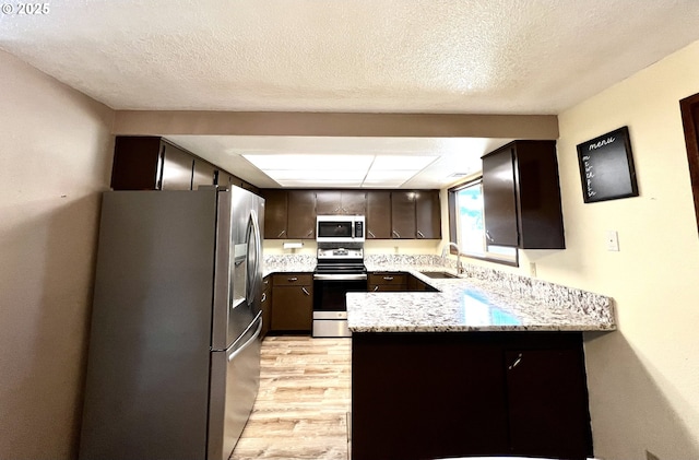 kitchen with a peninsula, a sink, stainless steel appliances, dark brown cabinets, and light wood-type flooring