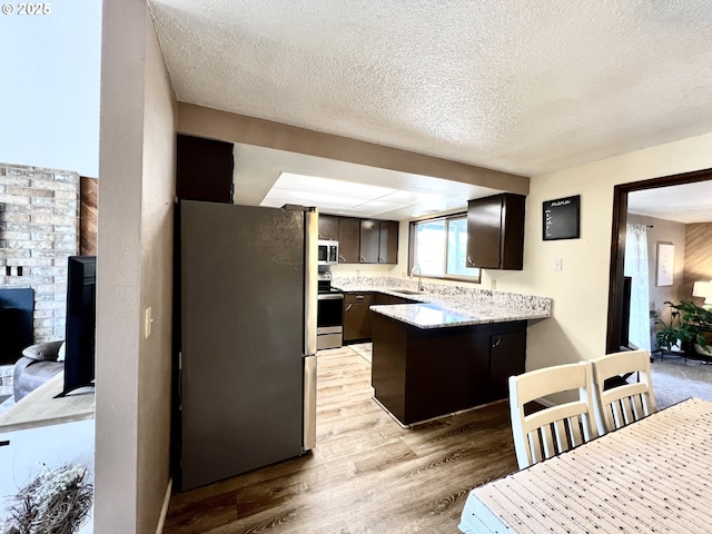 kitchen with dark brown cabinets, light countertops, light wood-style flooring, a peninsula, and stainless steel appliances