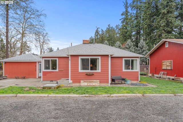 rear view of house featuring a yard, roof with shingles, a chimney, and a patio area