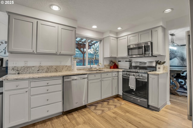 kitchen featuring sink, light hardwood / wood-style flooring, gray cabinets, appliances with stainless steel finishes, and light stone counters