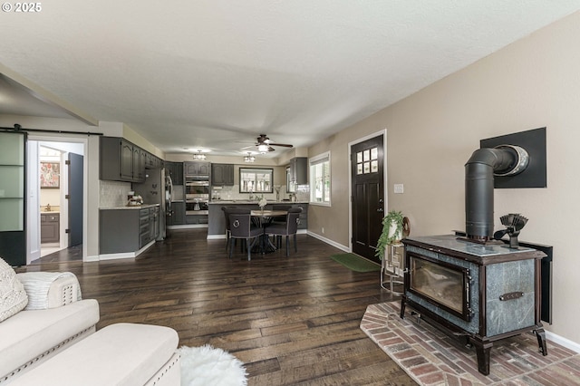 20256 S Swank Rd, Colton, OR 97017 - living area featuring a wood stove, dark wood-style flooring, baseboards, and ceiling fan