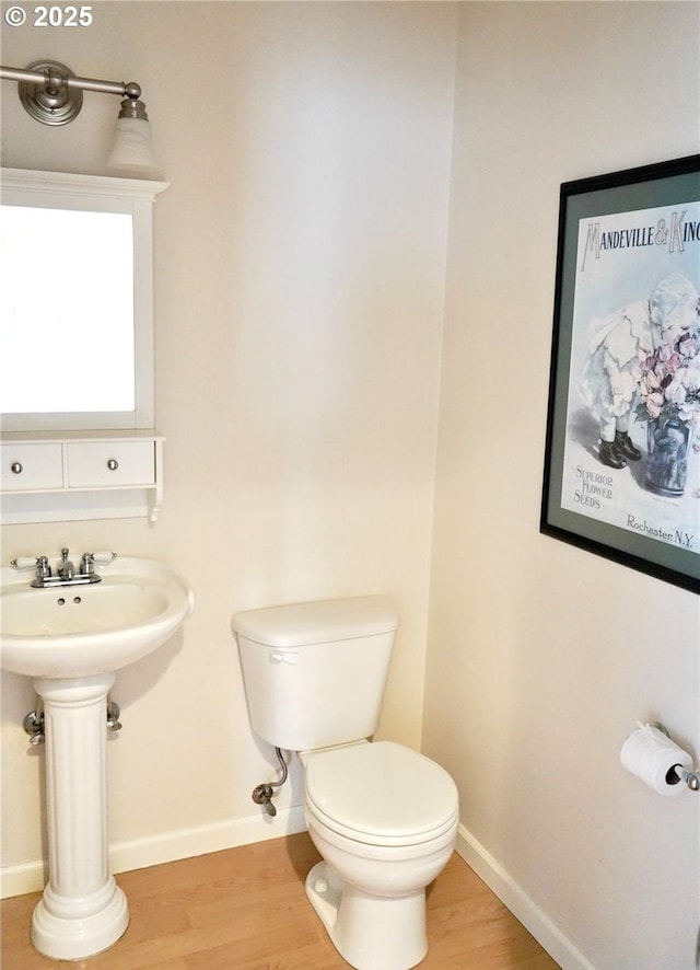 half bath with a sink, wood finished floors, toilet, and baseboards