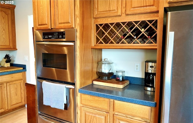 kitchen featuring stainless steel appliances, dark countertops, light wood-type flooring, and brown cabinets