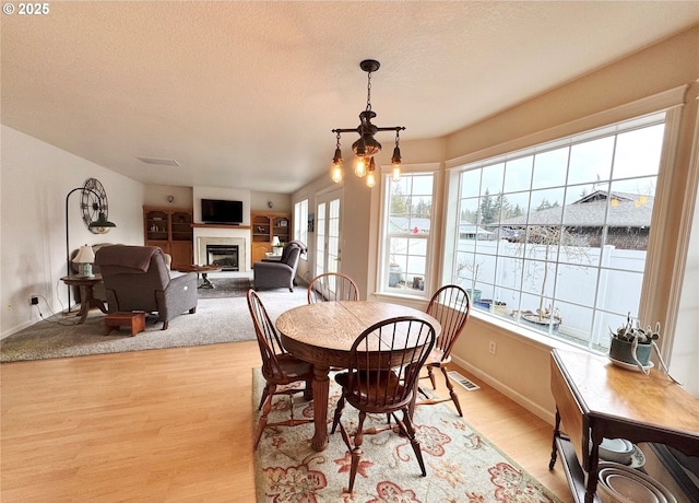 dining area featuring a textured ceiling, visible vents, baseboards, light wood-style floors, and a glass covered fireplace