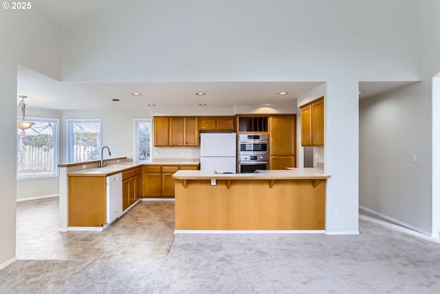 kitchen with a kitchen bar, light colored carpet, white appliances, and kitchen peninsula