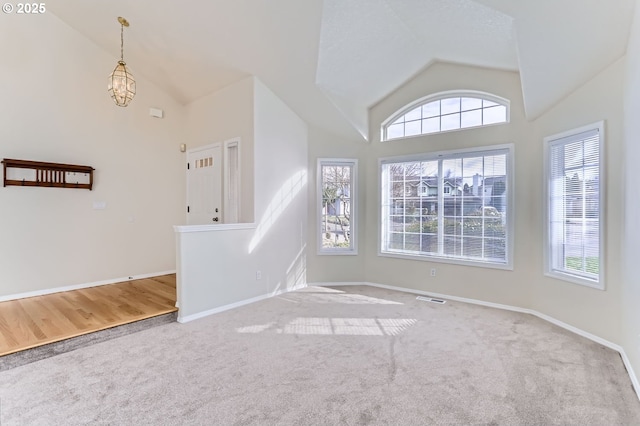 carpeted spare room with a chandelier and high vaulted ceiling