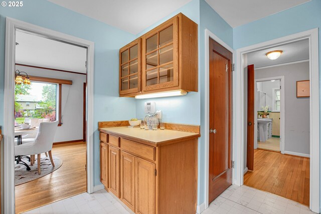 kitchen with light countertops, glass insert cabinets, baseboards, and light wood-style flooring