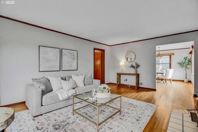living room featuring wood-type flooring, a chandelier, crown molding, and baseboards