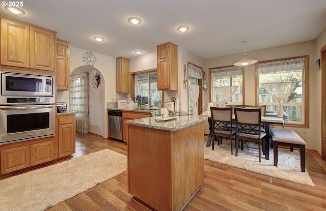 kitchen featuring light stone countertops, arched walkways, appliances with stainless steel finishes, light wood finished floors, and baseboards