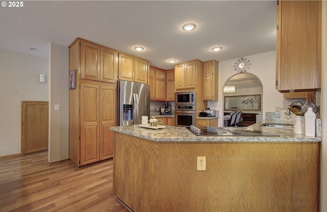 kitchen with light wood-style floors, a peninsula, light stone counters, a sink, and stainless steel appliances
