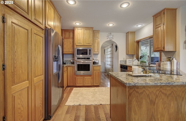 kitchen featuring light wood-style flooring, a peninsula, appliances with stainless steel finishes, light stone counters, and a sink