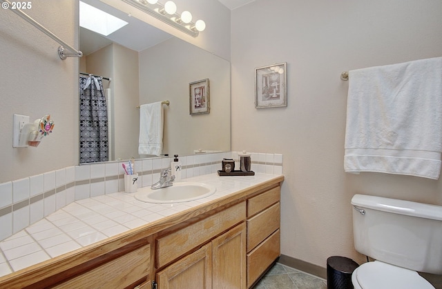 full bathroom featuring vanity, tile patterned flooring, toilet, a skylight, and baseboards