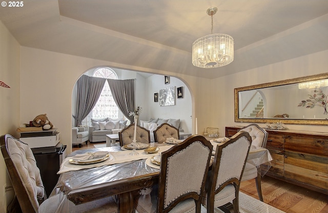 dining space featuring arched walkways, a notable chandelier, and wood finished floors