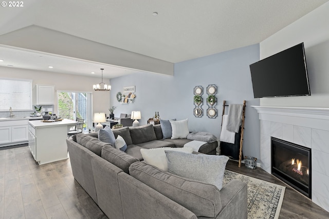 living room featuring a tiled fireplace, hardwood / wood-style flooring, sink, and a notable chandelier