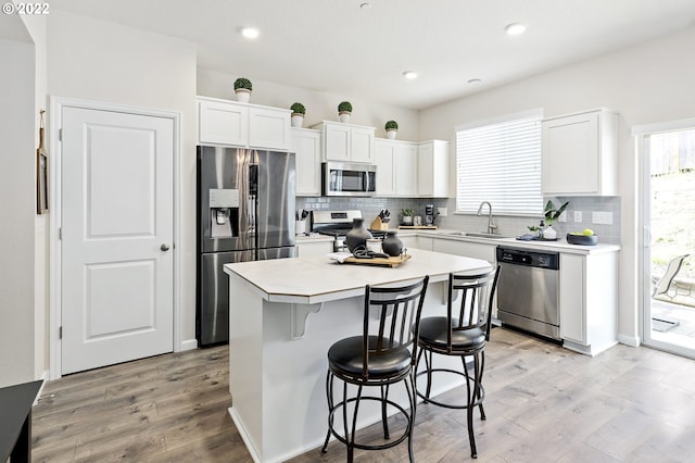 kitchen with a kitchen island, appliances with stainless steel finishes, white cabinets, backsplash, and light hardwood / wood-style flooring