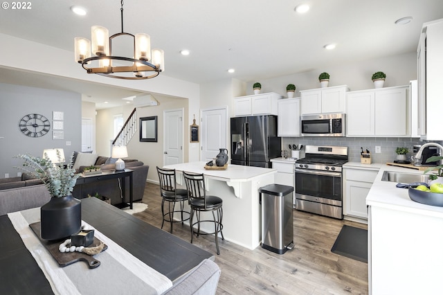 kitchen featuring a kitchen island, sink, white cabinets, hanging light fixtures, and stainless steel appliances