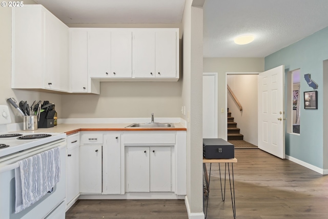 kitchen with white electric range oven, a sink, light countertops, white cabinetry, and wood finished floors