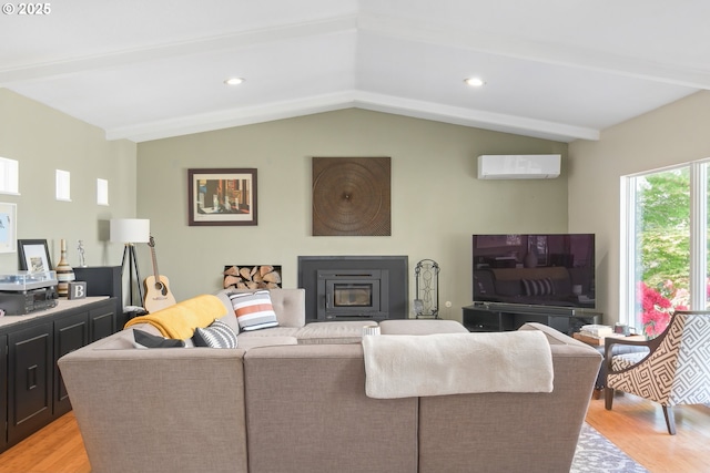 living room with light wood finished floors, a glass covered fireplace, a wall mounted AC, and vaulted ceiling