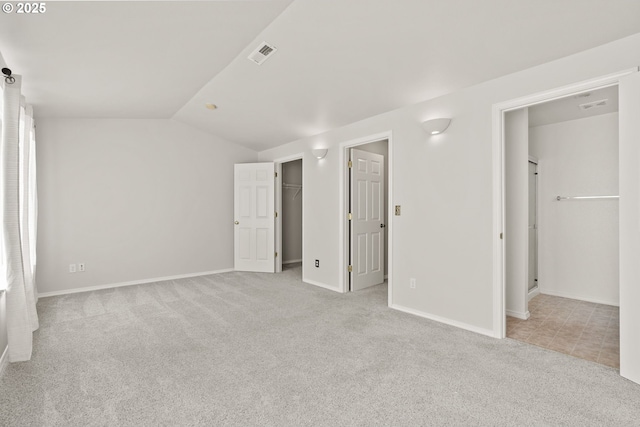 unfurnished bedroom featuring a spacious closet, light colored carpet, ensuite bathroom, and vaulted ceiling