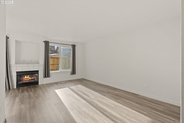 unfurnished living room featuring a tile fireplace and light hardwood / wood-style flooring