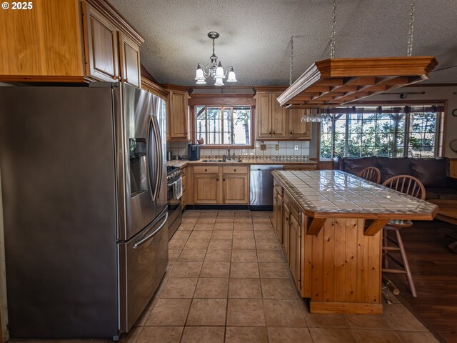 10160 NW Gordon Rd, Cornelius, OR 97113 - kitchen with appliances with stainless steel finishes, tile countertops, a chandelier, backsplash, and a kitchen breakfast bar