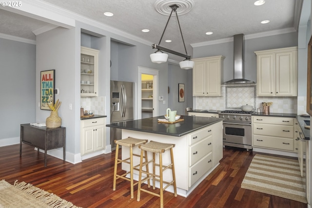 kitchen featuring dark wood finished floors, dark countertops, wall chimney exhaust hood, appliances with stainless steel finishes, and a center island