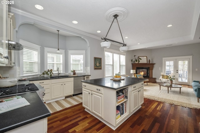 kitchen featuring dark countertops, a glass covered fireplace, open floor plan, a sink, and dishwasher