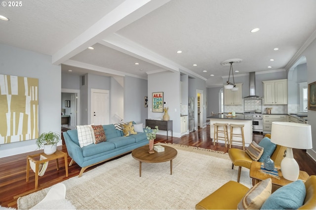 living room with dark wood-style flooring, beam ceiling, recessed lighting, ornamental molding, and baseboards