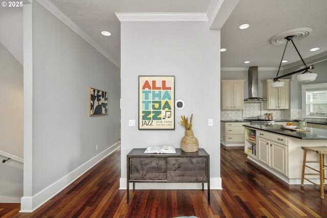 kitchen with dark wood-style flooring, cream cabinetry, wall chimney range hood, and decorative backsplash