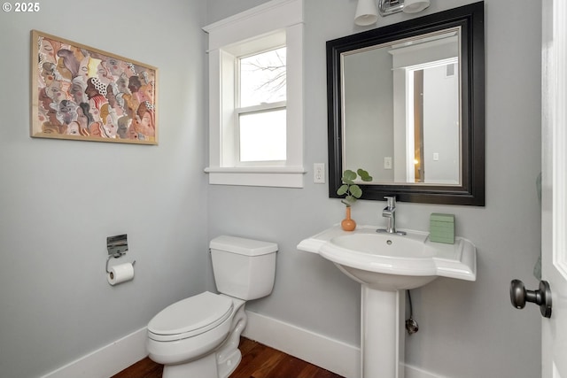 half bath with baseboards, toilet, and wood finished floors