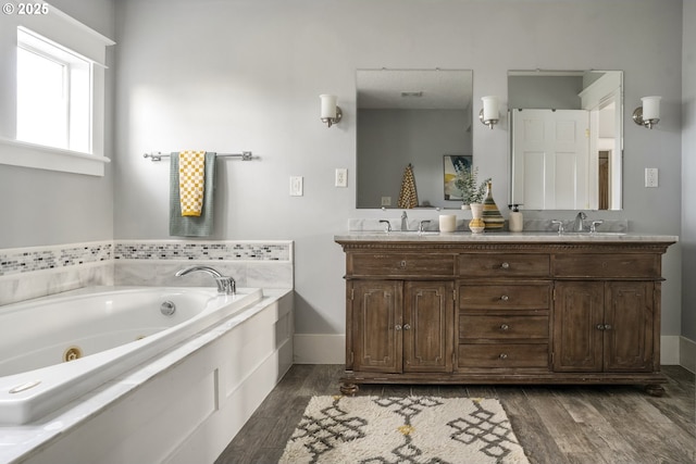 full bathroom featuring double vanity, a sink, a tub with jets, and wood finished floors