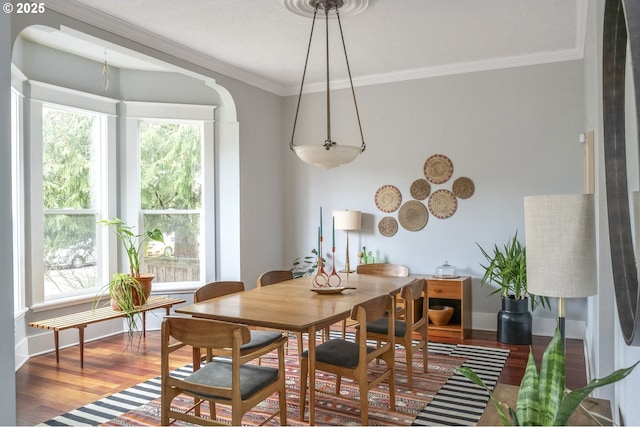 dining room featuring ornamental molding, arched walkways, baseboards, and wood finished floors