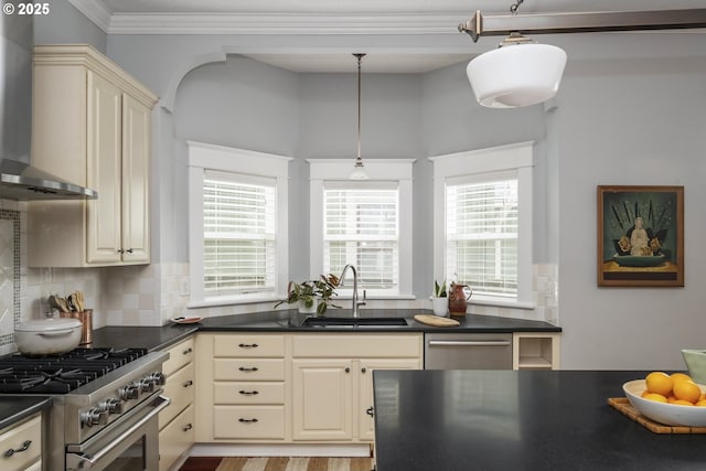 kitchen featuring dark countertops, wall chimney exhaust hood, high end stainless steel range oven, cream cabinetry, and a sink