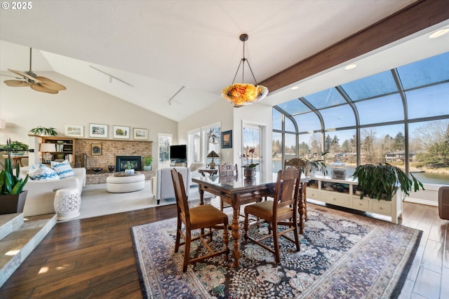 dining room with wood-type flooring, a brick fireplace, a sunroom, ceiling fan, and high vaulted ceiling