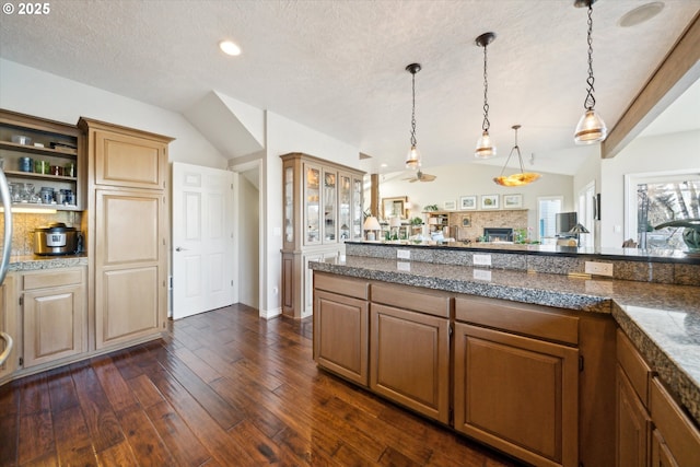 kitchen with pendant lighting, dark wood-style flooring, tile countertops, vaulted ceiling, and a lit fireplace