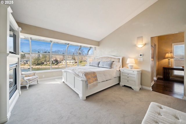 bedroom with baseboards, high vaulted ceiling, a glass covered fireplace, and light colored carpet