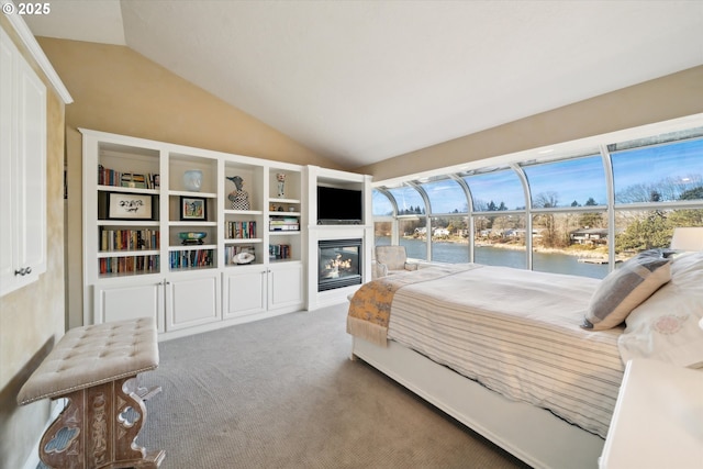 bedroom featuring carpet, a glass covered fireplace, and vaulted ceiling