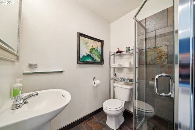 full bath with toilet, a stall shower, stone finish flooring, a sink, and baseboards