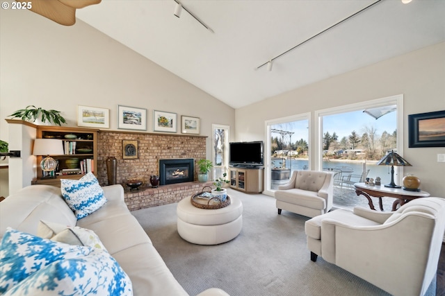 living room featuring high vaulted ceiling, a brick fireplace, carpet flooring, and rail lighting