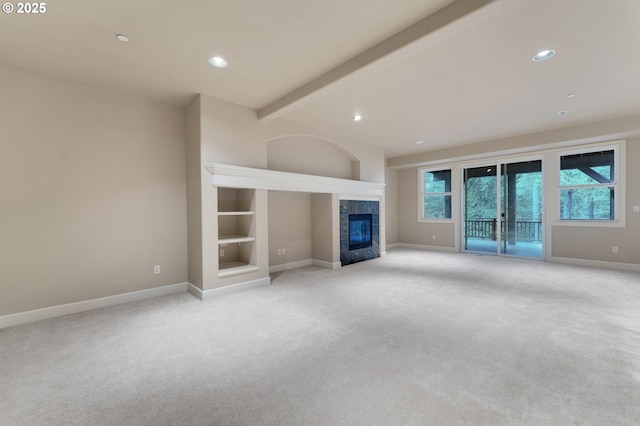 unfurnished living room with beam ceiling, a tile fireplace, and light colored carpet