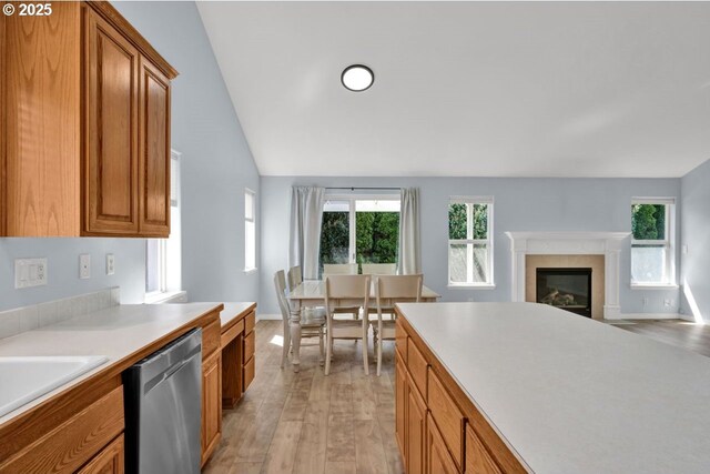 kitchen featuring dishwasher, light wood finished floors, brown cabinets, light countertops, and a glass covered fireplace