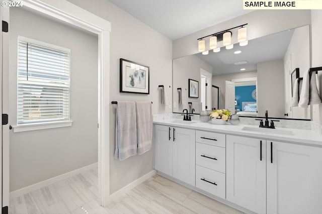 ensuite bathroom with baseboards, connected bathroom, a sink, and double vanity