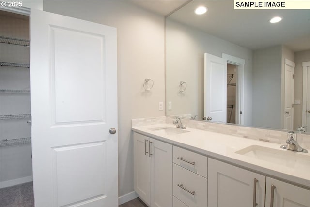 full bathroom featuring a spacious closet, double vanity, a sink, and recessed lighting