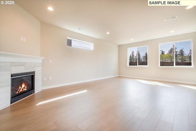 unfurnished living room with a healthy amount of sunlight, light wood-type flooring, visible vents, and a tiled fireplace