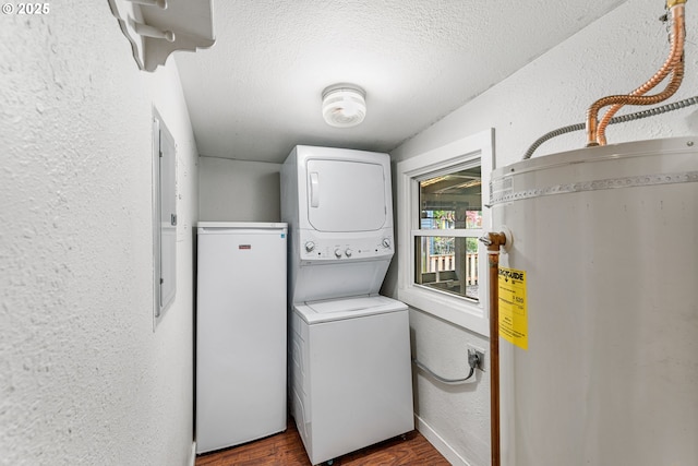 clothes washing area with water heater, a textured wall, stacked washer / drying machine, and laundry area