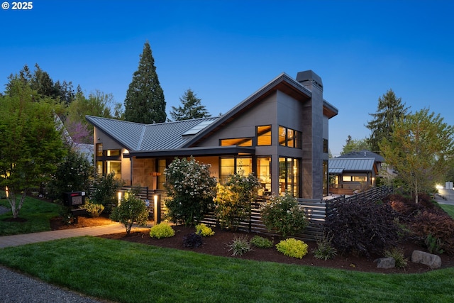 back of property featuring a lawn, a standing seam roof, a chimney, and metal roof