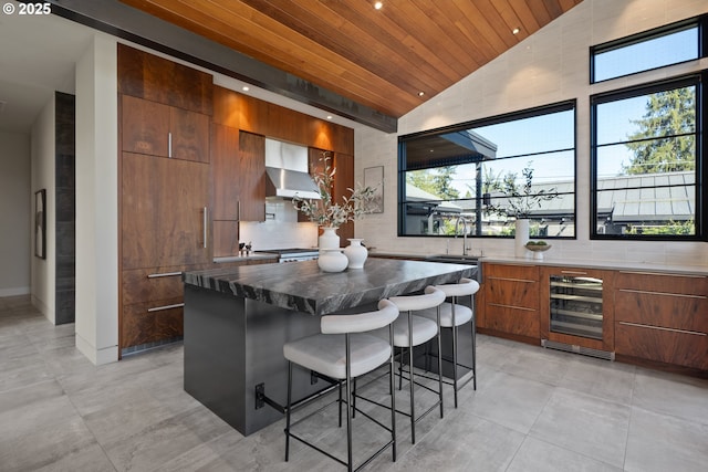 kitchen with wall chimney range hood, modern cabinets, lofted ceiling, and wine cooler