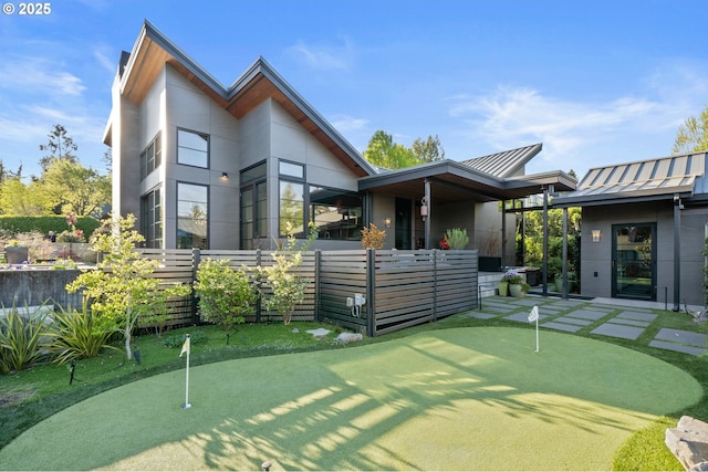 back of house featuring fence, a standing seam roof, and metal roof