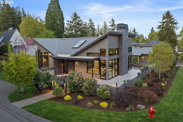 rear view of house with a standing seam roof, a chimney, a yard, and metal roof