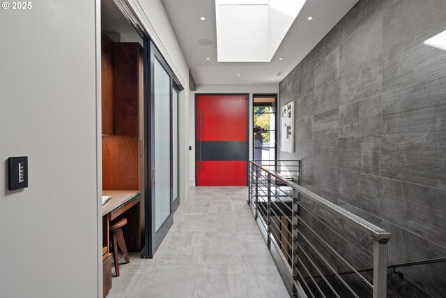 hallway featuring recessed lighting, a skylight, an upstairs landing, and tile walls